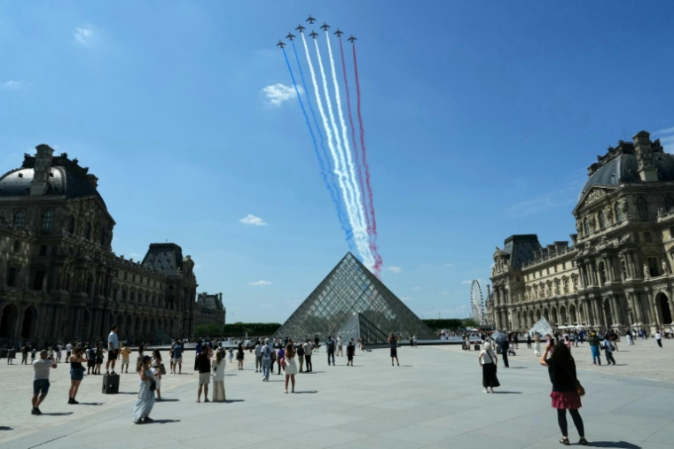 Des passants regardent la Patrouille de France (PAF) survoler la pyramide du Louvre conçue par l'architecte sino-américain Ieoh Ming Pei, le 9 juillet 2025 à Paris, lors d'une répétition du défilé annuel du 14 juillet ( AFP / Dimitar DILKOFF )