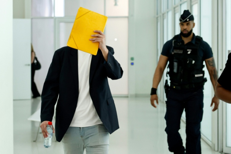 David G., un animateur périscolaire accusé d'agressions sexuelles sur des enfants d'école maternelle, cache son visage à son arrivée au tribunal de Paris, au premier jour de son procès, le 26 mai 2026 ( AFP / SIMON WOHLFAHRT )
