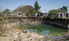 Des habitations surplombent une fosse à ciel ouvert creusée par des mineurs illégaux à la recherche de chrome à Bapong, un village minier de la province du Nord-Ouest (Afrique du Sud), le 25 août 2026 ( AFP / EMMANUEL CROSET )