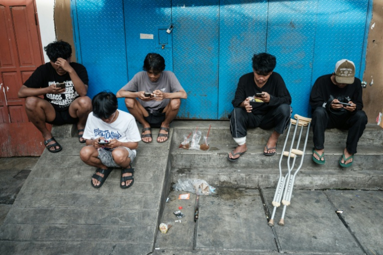 Des enfants utilisent leur smartphone à Jakarta le 26 mars 2026. ( AFP / YASUYOSHI CHIBA )
