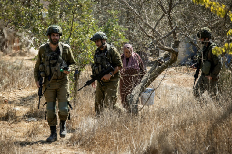 Des soldats israéliens escortent une Palestinienne dans un champ d'oliviers près de la colonie israélienne d'Elazar au sud de Bethléhem, en Cisjordanie occupée, le 17 octobre 2025 ( AFP / John Wessels )
