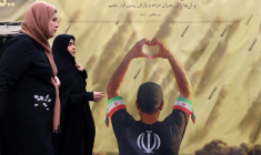 Des femmes passent devant une banderole représentant un homme faisant un cœur avec ses mains devant des tirs de missiles, à Téhéran le 19 avril 2026 ( AFP / ATTA KENARE )