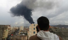 Un journaliste prend une photo de la fumée noire qui s'élève après une frappe israélienne sur Sanaa, la capitale du Yémen tenue par les rebelles houthis, le 24 août 2025 ( AFP / Mohammed HUWAIS )