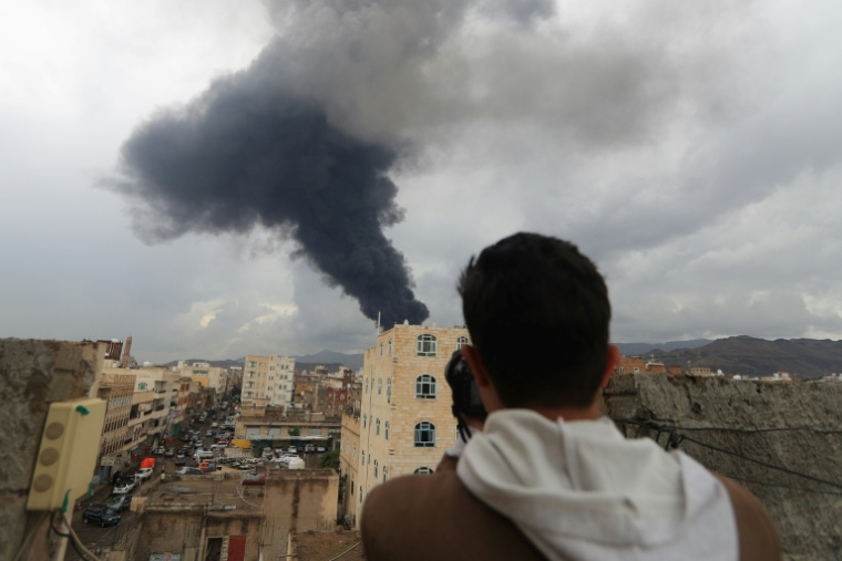 Un journaliste prend une photo de la fumée noire qui s'élève après une frappe israélienne sur Sanaa, la capitale du Yémen tenue par les rebelles houthis, le 24 août 2025 ( AFP / Mohammed HUWAIS )