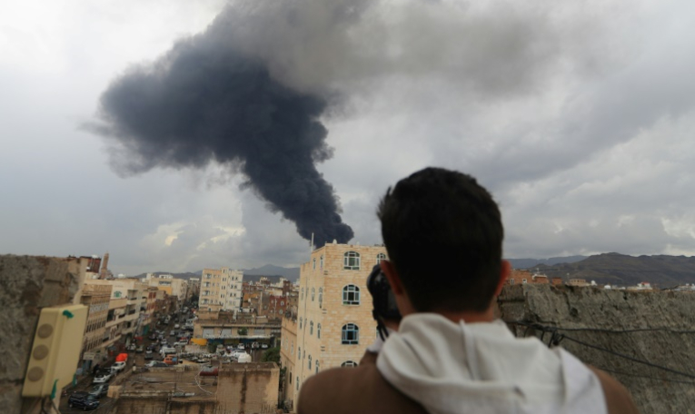 Un journaliste prend une photo de la fumée noire qui s'élève après une frappe israélienne sur Sanaa, la capitale du Yémen tenue par les rebelles houthis, le 24 août 2025 ( AFP / Mohammed HUWAIS )