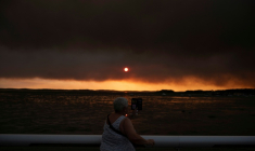 Une femme observe la fumée depuis la plage à Andernos-les-Bains lors d'un incendie dans la forêt de Lège-Cap-Ferret, dans le sud-ouest de la France, le 23 juillet 2026, alors qu'une partie de la zone voisine a été évacuée ( AFP / Olivier MORIN )