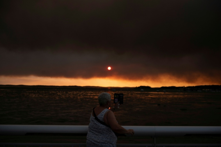 Une femme observe la fumée depuis la plage à Andernos-les-Bains lors d'un incendie dans la forêt de Lège-Cap-Ferret, dans le sud-ouest de la France, le 23 juillet 2026, alors qu'une partie de la zone voisine a été évacuée ( AFP / Olivier MORIN )