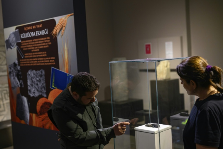 Les archéologues Murat Türkteki, à gauche, et Deniz Sari, à droite, observent un pain carbonisé vieux de 5.000 ans exposé au musée archéologique d'Eskisehir, en Turquie, le 23 mai 2025 ( AFP / Yasin AKGUL )