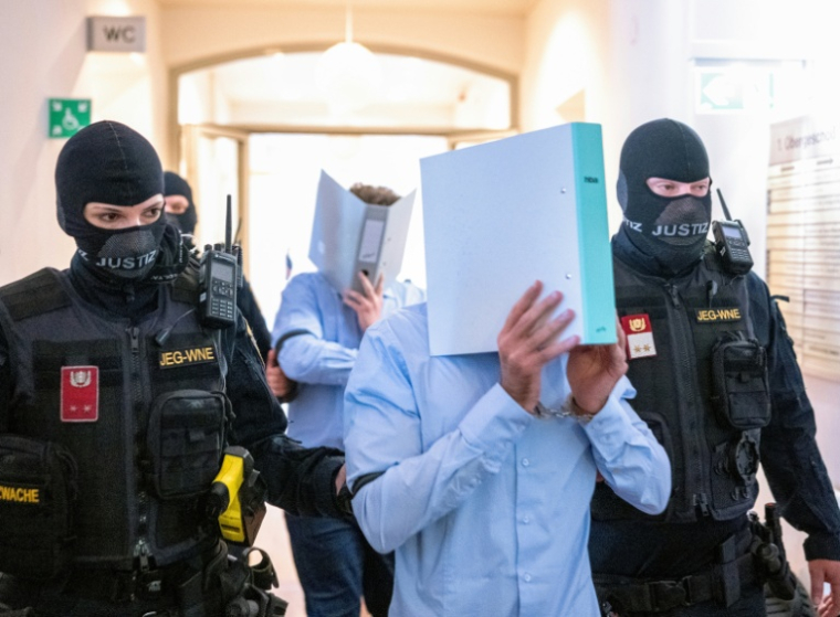 Des prévenus cachent leurs visages derrière un dossier, escortés par des policiers vers la salle d'audience du tribunal de Wiener Neustadt, le 28 mai 2026 en Atriche, lors du procès pour un complot contre un concert de la star américaine Taylor Swift à Vienne ( AFP / Joe Klamar )