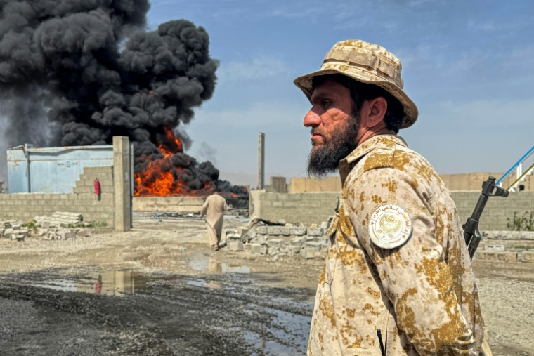 Un membre des forces de sécurité talibanes monte la garde alors que de la fumée s'élève du site de frappes aériennes pakistanaises sur des dépôts pétroliers, près de l'aéroport de Kandahar, le 13 mars 2026 en Afghanistan ( AFP / STR )