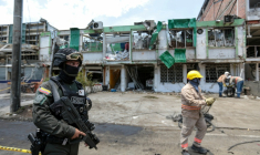 Un membre du Groupe des opérations spéciales de la police nationale colombienne monte la garde tandis que des agents de nettoyage déblayent les débris du site d'une explosion à la bombe survenue la veille à Cali, en Colombie, le 22 août 2025 ( AFP / Iusef Samir Rojas )