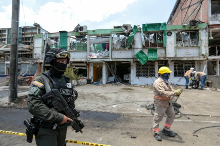 Un membre du Groupe des opérations spéciales de la police nationale colombienne monte la garde tandis que des agents de nettoyage déblayent les débris du site d'une explosion à la bombe survenue la veille à Cali, en Colombie, le 22 août 2025 ( AFP / Iusef Samir Rojas )