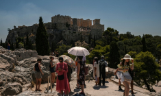 Des touristes se protègent du soleil en face de la colline de l'Acropole à Athènes, le 8 juillet 2025 en Grèce ( AFP / Aris MESSINIS )