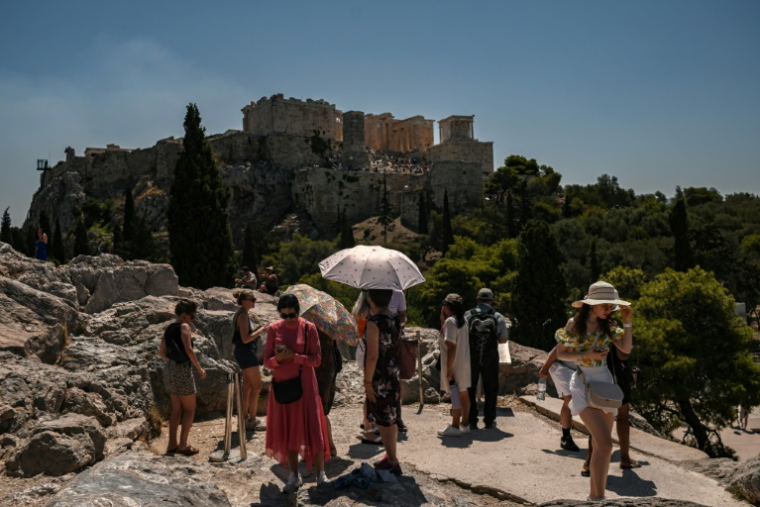 Des touristes se protègent du soleil en face de la colline de l'Acropole à Athènes, le 8 juillet 2025 en Grèce ( AFP / Aris MESSINIS )