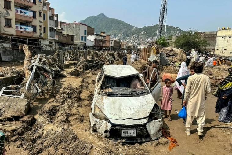 Des habitants de Mingora sont réunis autour d'un véhicule endommagé et de débris après l'effondrement de la route après les crues subites dans la province montagneuse de Khyber Pakhtunkhwa au Pakistan le 16 août 2025 ( AFP / Mehboob UL HAQ )