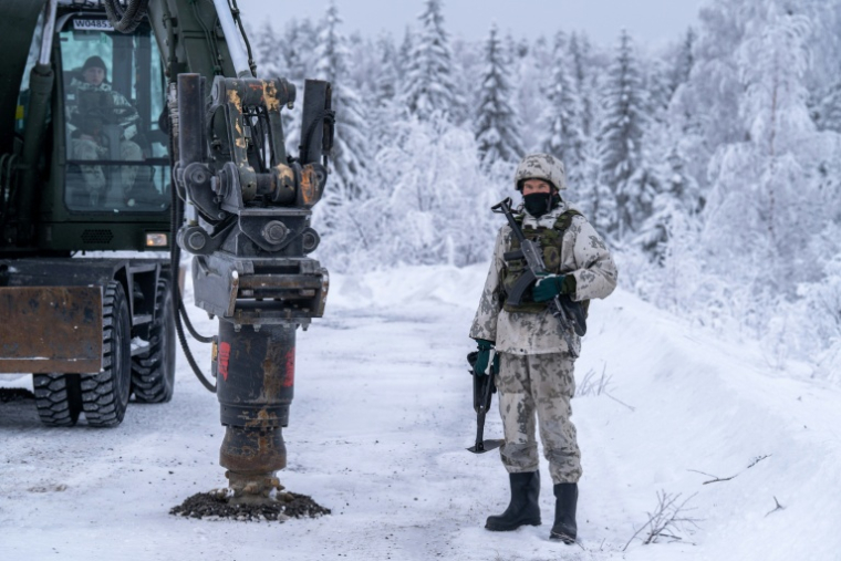 Un militaire finlandais à côté d'une excavatrice qui creuse l’asphalte gelé pour enfouir des mines antichars d’exercice, à Kajaani, en Finlande, le 3 février 2026 ( AFP / Alessandro RAMPAZZO )