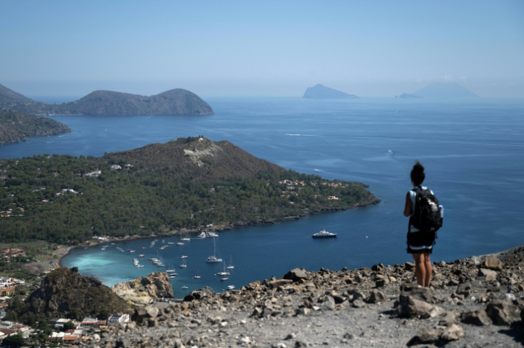 Une touriste sur le bord du cratère de La Fossa, sur l'île de Vulcano, avec (g-d) les îles de Lipari, Panarea et Stromboli, dans l'archipel des Éoliennes, au large de la Sicile, le 9 juillet 2026 en Italie ( AFP / Marco Bertorello )