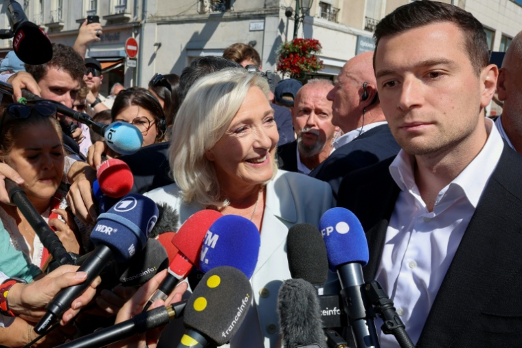 Marine Le Pen (c), cheffe du groupe parlementaire Rassemblement national (RN) et candidate à la présidentielle de 2027, et Jordan Bardella, président du RN, entourés de journalistes à leur arrivée à La Flèche pour un rassemblement de campagne, le 8 juillet 2026 dans la Sarthe ( AFP / FRED TANNEAU )
