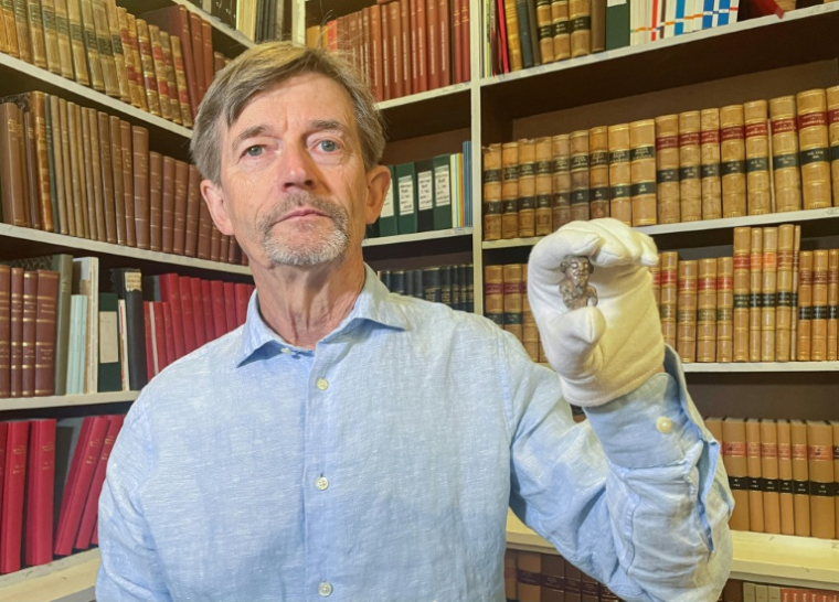 Le conservateur du musée national du Danemark, Peter Pentz, montre une figurine en ivoire de morse, pièce d'un jeu de société, qui serait le premier portrait d'un Viking, le 26 août 2025 à Copenhague ( AFP / Camille BAS-WOHLERT )