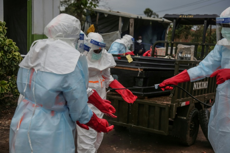 Du personnel médical en combinaison de protection se désinfectent les gants après avoir enterré un patient à Rwampara le 21 mai 2026 en République démocratique du Congo ( AFP / Seros MUYISA )