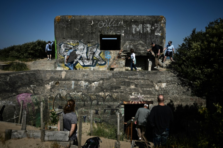 Des touristes devant les vestiges d'un blockhaus de la Seconde Guerre mondiale désormais recouvert de graffitis, sur la côte atlantique à Soulac-sur-Mer, en Gironde, le 15 mai 2025 ( AFP / Philippe LOPEZ )