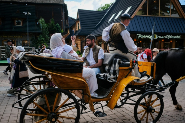 Des touristes se prennent en photo dans une calèche dans les rues de Zakopane, en Pologne, le 4 août 2025 ( AFP / BARTOSZ SIEDLIK )