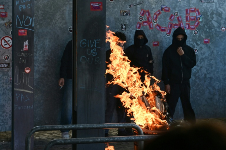 Des manifestants masqués se tiennent près d'une barricade en feu lors d'une manifestation à Liège, le 6 octobre 2026, contre les réformes de l'enseignement en Belgique francophone ( AFP / Nicolas TUCAT )