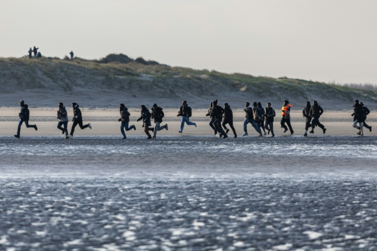 Des migrants courent pour embarquer sur un bateau de passeurs et tenter de traverser la Manche au large de la plage de Gravelines, dans le Nord, le 3 mars 2026 ( AFP / Sameer Al-DOUMY )
