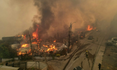 Sur cette vue aérienne, de la fumée et des flammes s’échappent de maisons en feu lors d’un incendie de forêt à Concepción, au Chili, le 18 janvier 2026 ( AFP / GUILLERMO SALGADO )