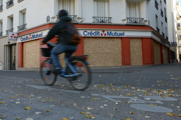 Un cycliste passe devant une banque barricadée par des plaques de bois à Paris le 30 octobre 2026 ( AFP / Thomas SAMSON )