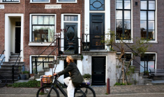 Une femme passe à vélo devant une maison traditionnelle d'Amsterdam