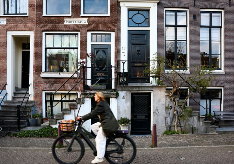 Une femme passe à vélo devant une maison traditionnelle d'Amsterdam