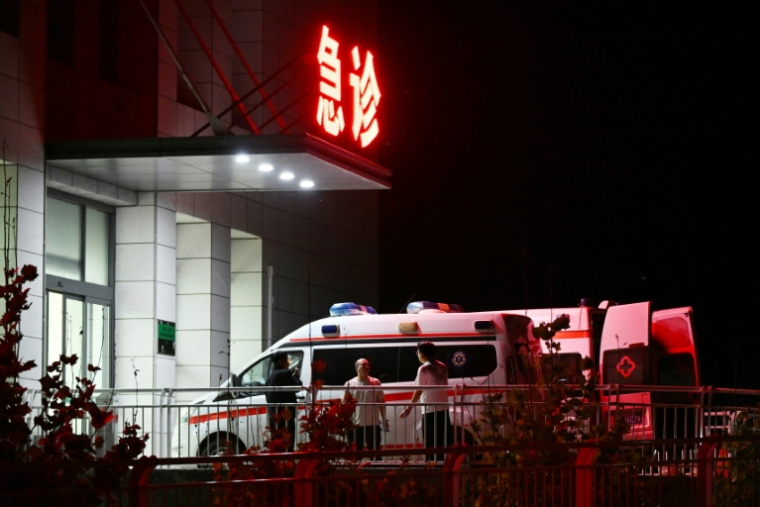 Des hommes se tiennent près d'ambulances à l'hôpital de Qinyuan (nord de la Chine), bouclé par un cordon de sécurité, qui est proche de la mine de charbon de Liushenyu où des dizaines de mineurs ont été tués dans une explosion, le 24 mai 2026 ( AFP / GREG BAKER )