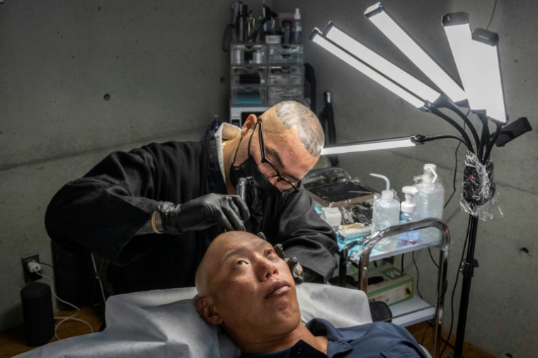 Remy, tatoueur professionnel, réalise une intervention de micropigmentation du cuir chevelu sur un client, dans son studio de Ginowan, à Okinawa au Japon, le 19 mai 2026 ( AFP / Yuichi YAMAZAKI )