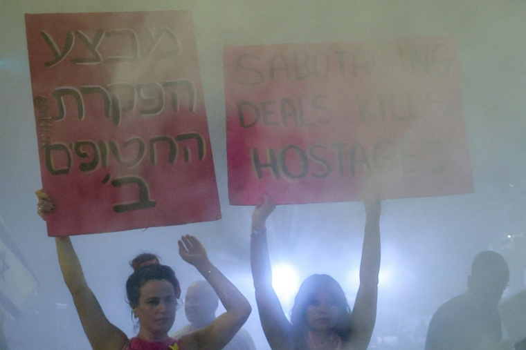 Des manifestants brandissent des pancartes au milieu des fumées d'extincteurs lors d'une manifestation organisée par les familles des Israéliens retenus en otages dans la bande de Gaza, devant le ministère de la Défense à Tel-Aviv, le 23 août 2025 ( AFP / Jack GUEZ )