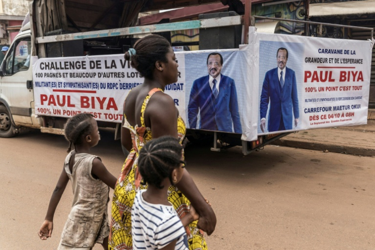 Une femme et ses enfants traversent la rue près d'un camion de campagne du président sortant du Cameroun, Paul Biya, à Yaoundé le 11 octobre 2025 ( AFP / MARCO LONGARI )