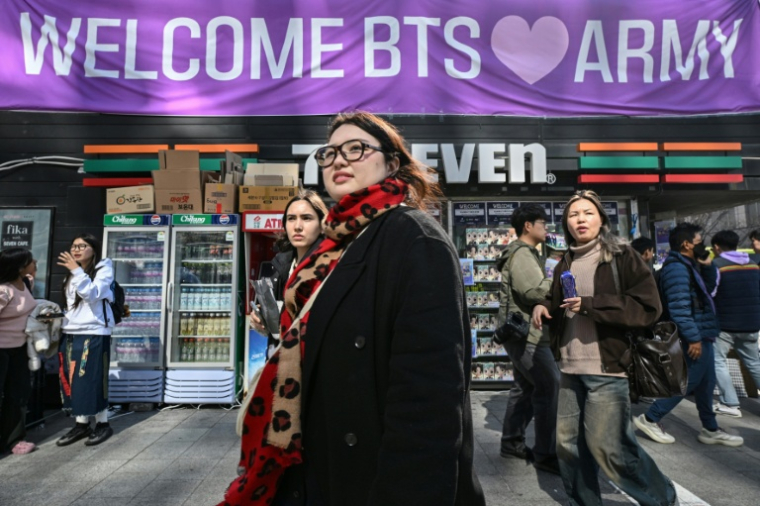 Des passants défilent devant une supérette ornée d'une bannière souhaitant la bienvenue aux fans de BTS, à proximité du lieu du concert de retour du boys band de K-pop BTS, dans le centre-ville de Séoul, le 21 mars 2026 ( AFP / Jung Yeon-je )