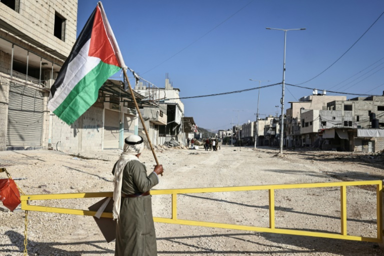Un homme tenant un drapeau palestinien devant l'entrée du camp de réfugiés de Nur Shams, à coté de Tulkarem, le 18 novembre 2025 ( AFP / Zain JAAFAR )