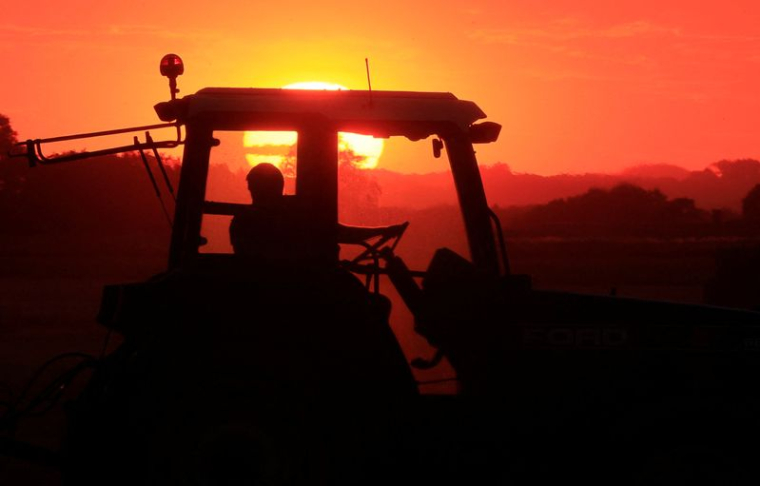 Après avoir récolté son champ de blé, un agriculteur ramasse la paille au coucher du soleil pour former des balles, à Haynecourt