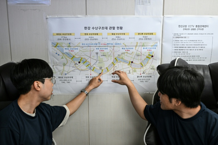 Deux membres du personnel du Centre de contrôle intégré de la vidéosurveillance du pont Hangang consultent une carte pour indiquer la position des équipes de secours sur le fleuve Han, à Séoul, le 24 juin 2026 ( AFP / Jade GAO )