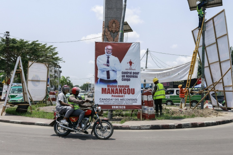 Des motocyclistes passent devant une affiche électorale de Vivien Romain Manangou, candidat indépendant à la présidence congolaise et professeur de droit public à l'université, à Brazzaville, le 12 mars 2026 ( AFP / Daniel BELOUMOU OLOMO )