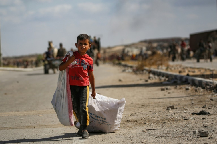 Un garçon palestinien porte un sac et traîne un autre derrière lui alors qu'il revient d'un point de distribution alimentaire dans le centre de la bande de Gaza, le 5 octobre 2025 ( AFP / Eyad BABA )