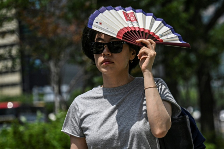 Une femme s'abrite le visage du soleil avec un éventail, le 12 juillet 2026 à Séoul   ( AFP / JADE GAO )