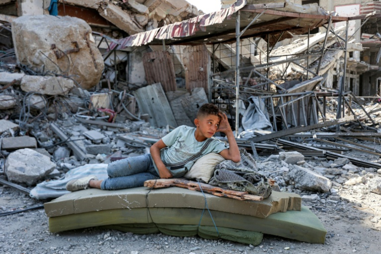 Un jeune Palestinien se repose dans les décombres de Khan Younès, dans le sud de la bande de Gaza, le 10 octobre 2025 ( AFP / Omar AL-QATTAA )
