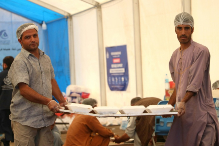 Deux bénévoles distribuant des plats à leurs compatriotes expulsés d'Iran, au poste frontière d'Islam Qala, dans la province de Hérat, en Afghanistan, le 24 juillet 2025 ( AFP / Mohsen KARIMI )