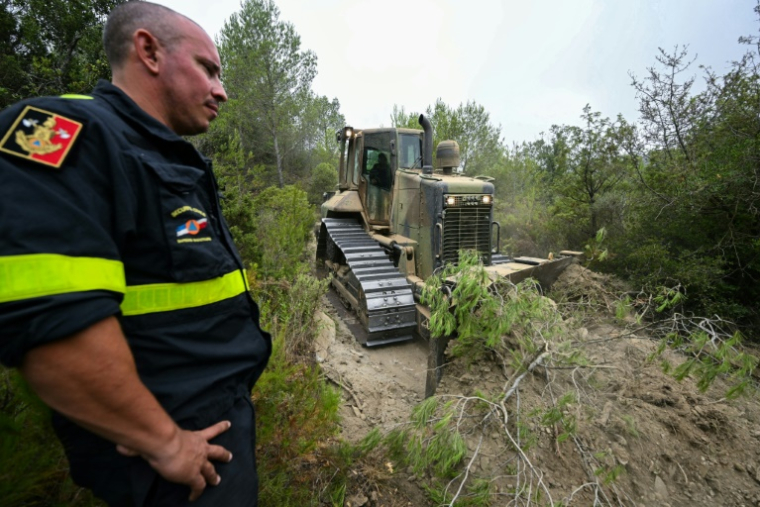 Un membre de la Sécurité civile se tient près d'un bulldozer qui élargit un sentier afin de faciliter l'accès des pompiers en cas d'incendie, le 8 août 2025 près de Talairan, dans l'Aude ( AFP / Bertrand GUAY )