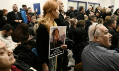Une femme porte le portrait d'une proche décédée dans la collision ferroviaire la plus meurtrière de Grèce alors que s'ouvre le procès de 36 personnes, le 23 mars 2026 sur le campus universitaire de Larissa ( AFP / Sakis Mitrolidis )