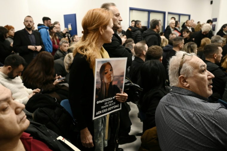 Une femme porte le portrait d'une proche décédée dans la collision ferroviaire la plus meurtrière de Grèce alors que s'ouvre le procès de 36 personnes, le 23 mars 2026 sur le campus universitaire de Larissa ( AFP / Sakis Mitrolidis )