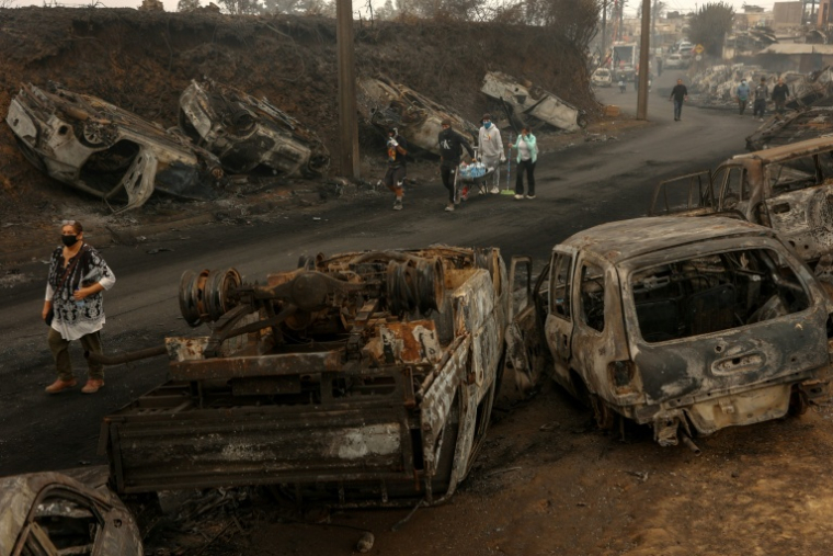 Des habitants marchent dans une rue jonchée de carcasses calcinées de véhicules après qu'un incendie de forêt a ravagé Lirquen, près de Concepcion, au Chili, le 20 janvier 2026 ( AFP / Raul BRAVO )