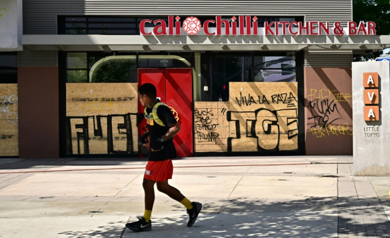 Un passant devant des commerces barricadés et recouverts de graffitis, dans le centre-ville de Los Angeles, le 17 juin 2025 ( AFP / Frederic J. BROWN )